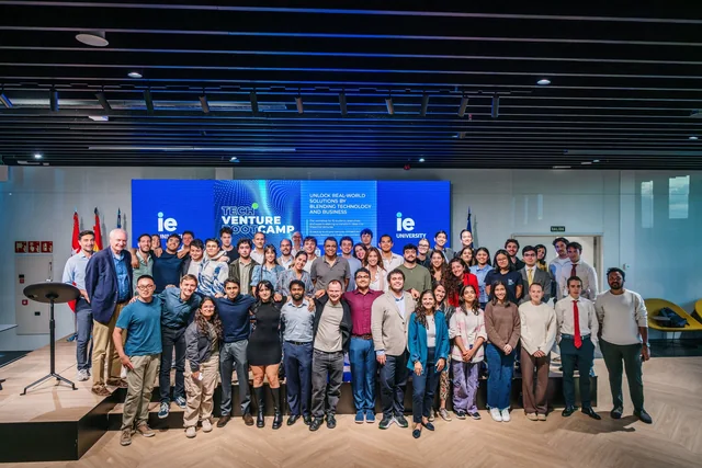 Participants posing on stage in front of IE Tech Venture Bootcamp screens.